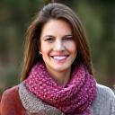 Portrait of Sarah, smiling while holding a knitted scarf