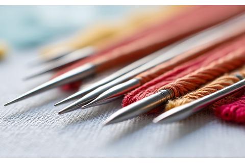 Assortment of cross-stitch needles of different lengths and point types, alongside embroidery floss.